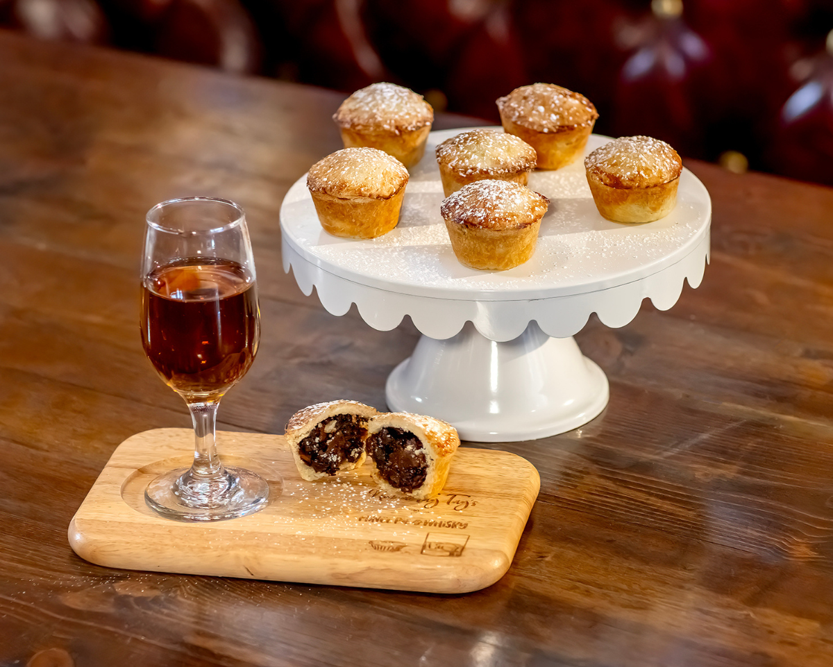 6 ready to eat mince pies with a glass of whiskey and one cut mince pie showing filling