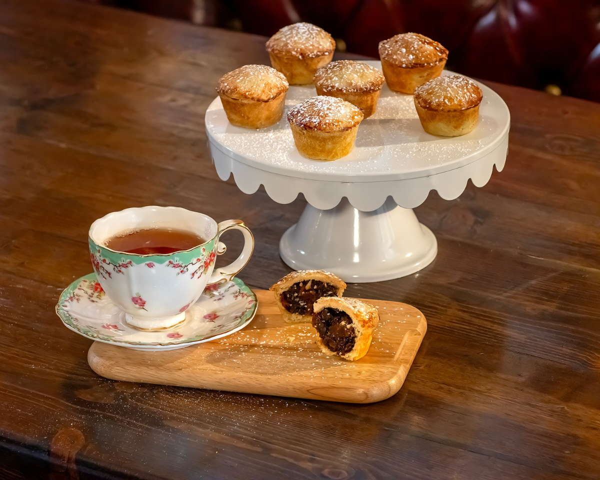 6 ready to eat mince pies with a cup of tea and one mince pie cut in half to showing filling