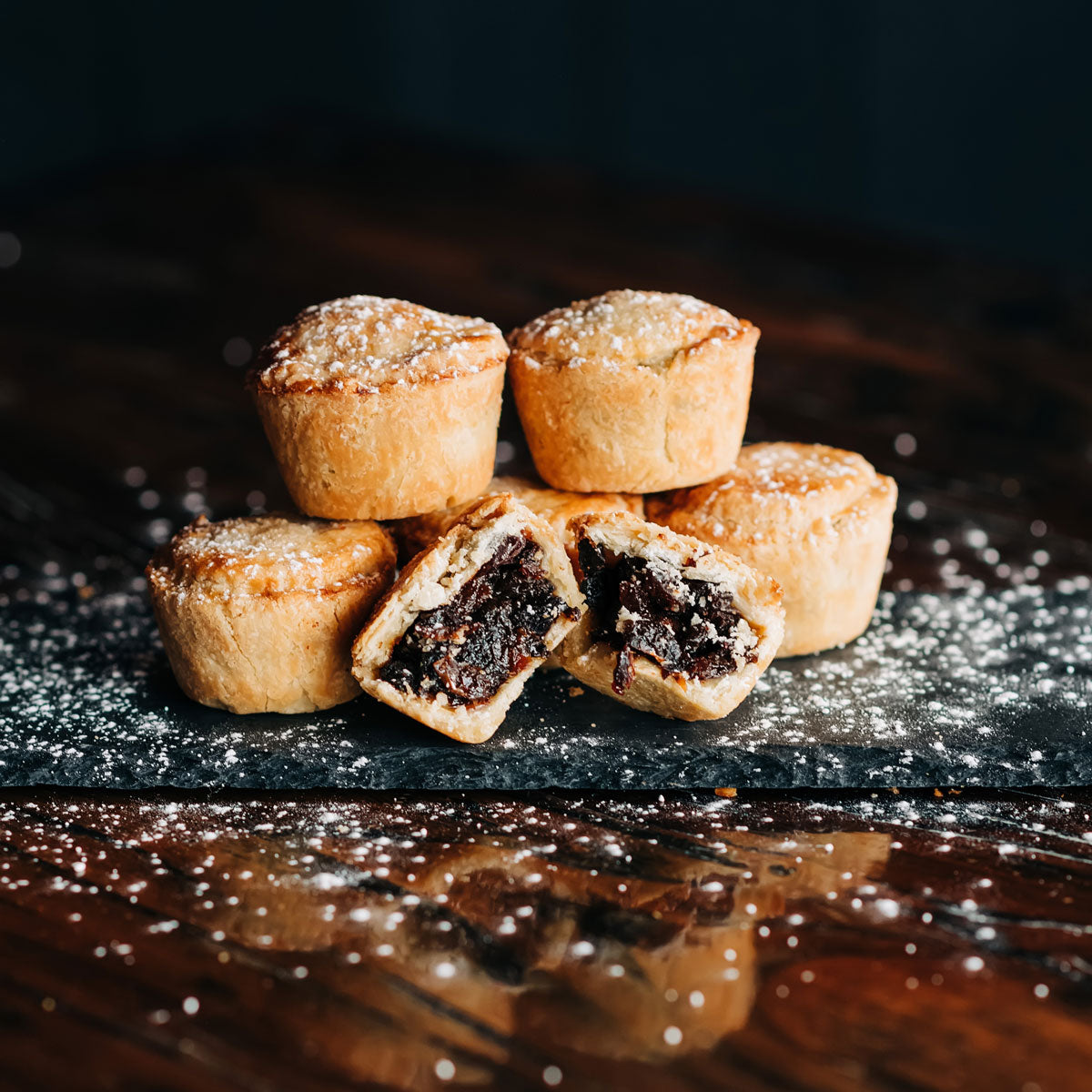 Gourmet mince pies sprinkled with powdered sugar. One pie is broken open to reveal the mince filling.