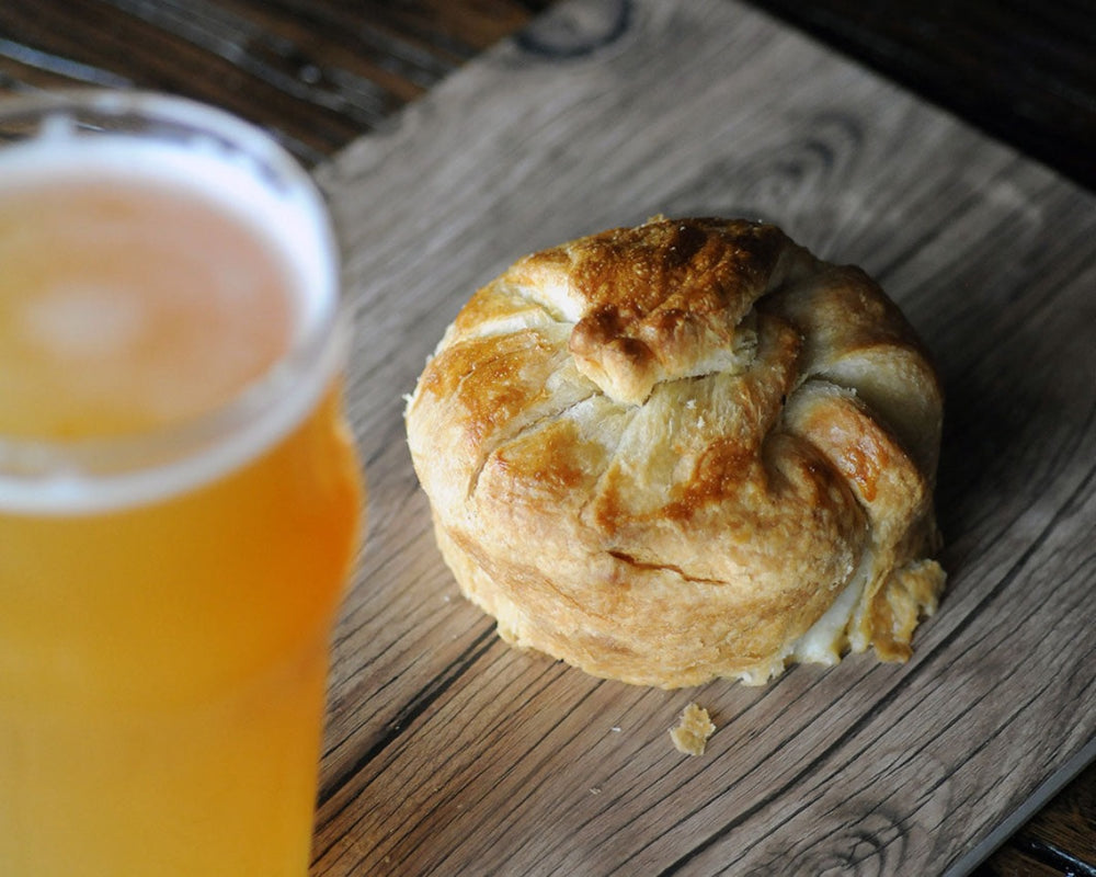 A golden chicken bacon cheese pasty ready for eating and served beside a pint of ale